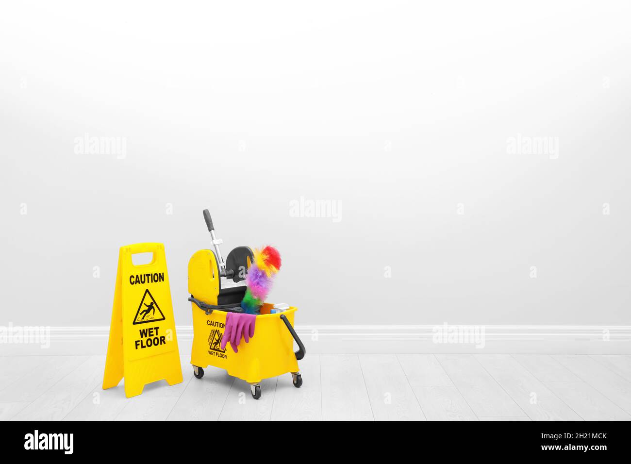 Safety sign with phrase "CAUTION WET FLOOR" and mop bucket on floor