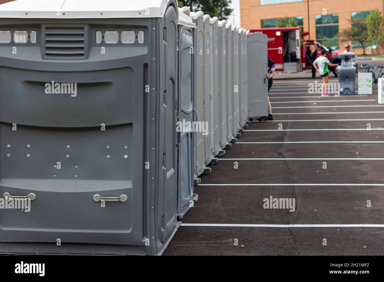 A line up of many grey portable toilets at a parking lot to be used by a crowd of people during an event or festival. These ensure people have access Stock Photo