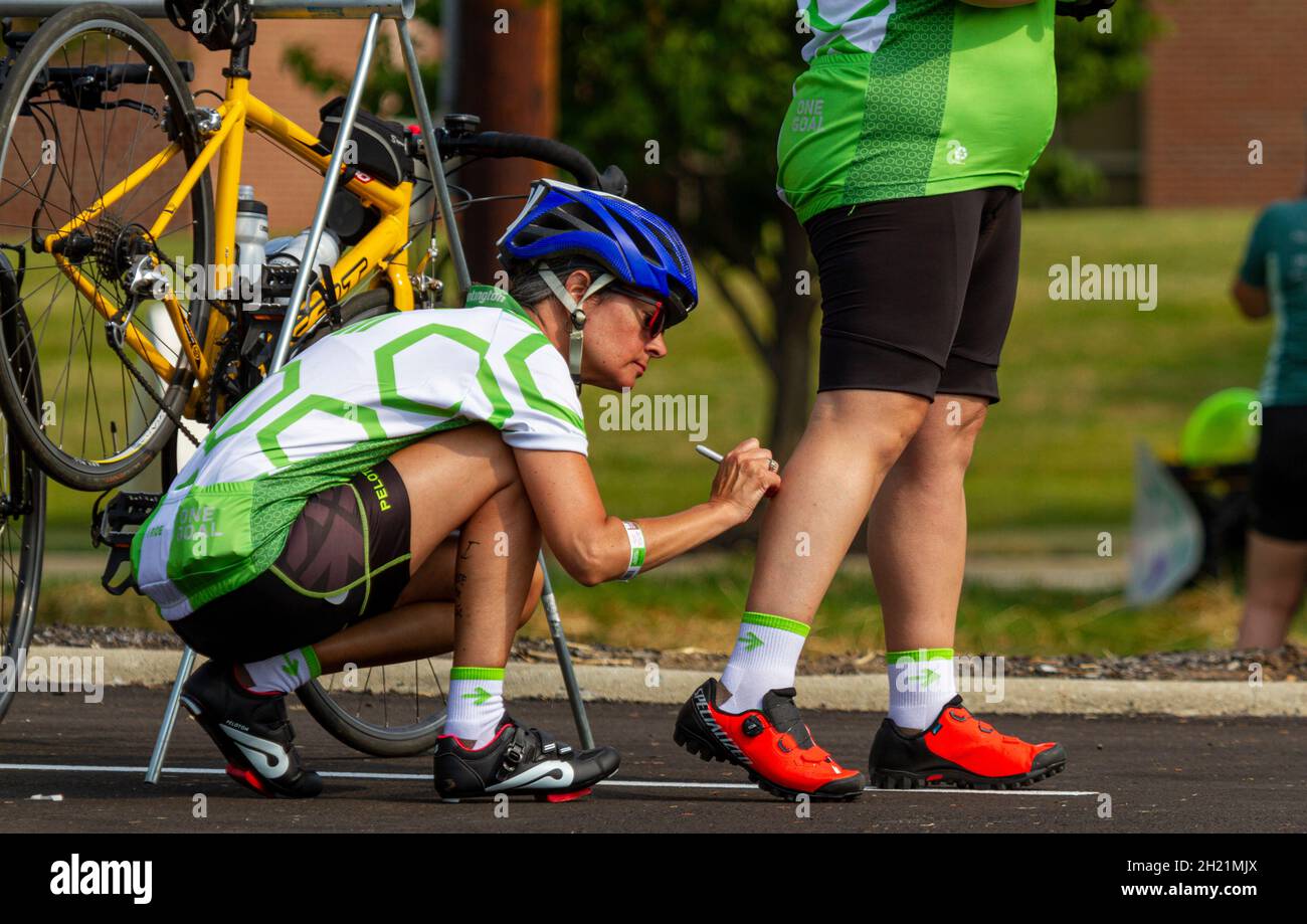 Columbus, OH USA 08-07-2021: A young caucasian woman wearing cycling suits and helmet is writing something on the leg of her teammate for support or l Stock Photo