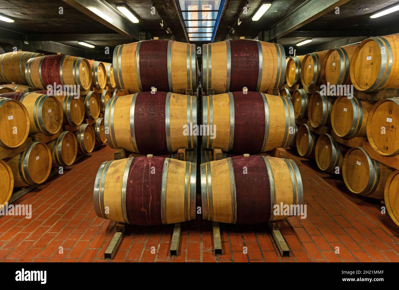 Wine aging in oak wooden casks in the cellar of a winery with vineyard, Stellenbosch, South Africa. Stock Photo
