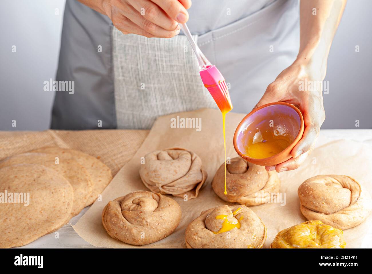 closeup isolated image of a caucasian woman preparing sweet Turkish pastry rolls with tahini and petimezi. She spreads egg yolk on top using slicon br Stock Photo