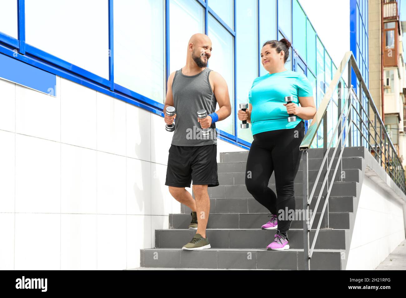 Overweight man and woman running with dumbbells on stairs outdoors