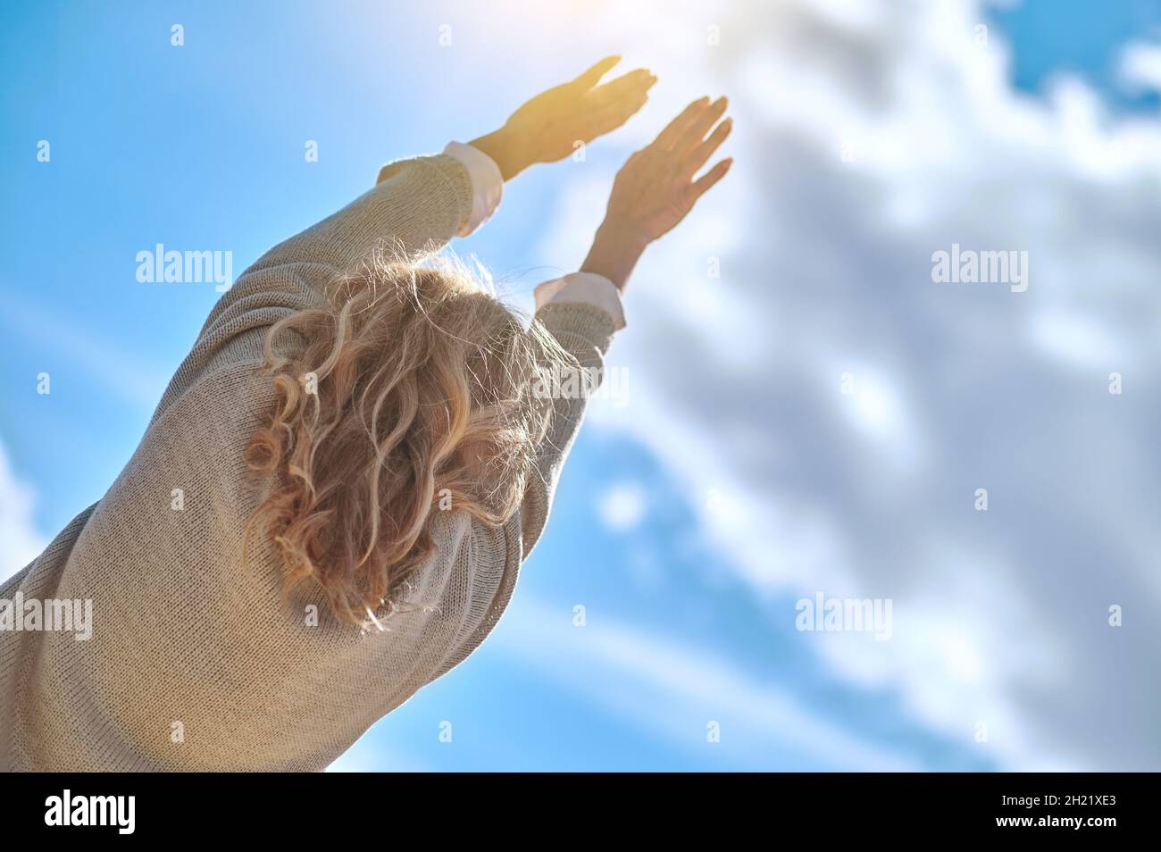 View back of woman stretching hands towards sun Stock Photo