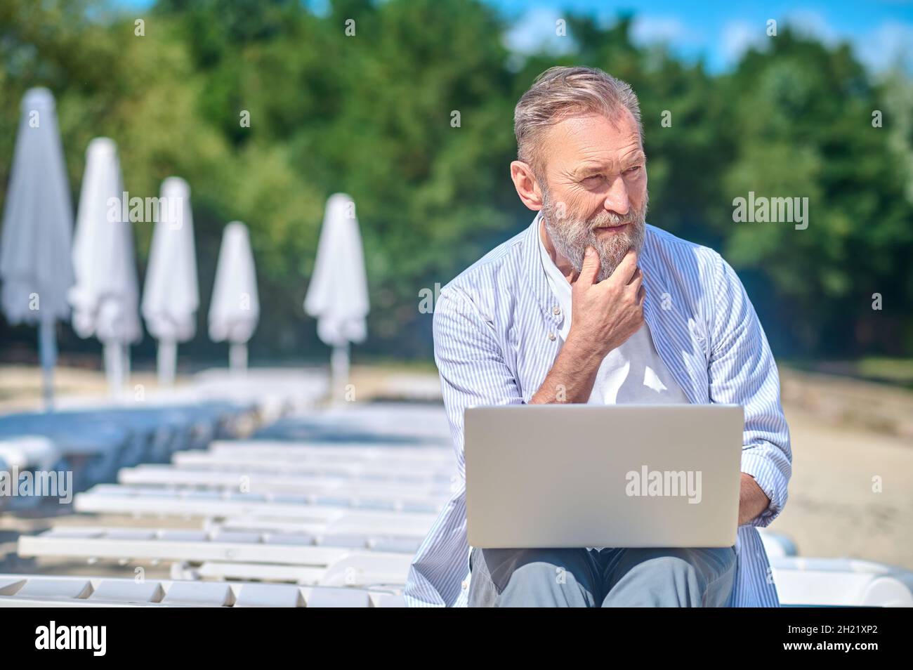 Pensive man with laptop sitting on beach lounger Stock Photo - Alamy
