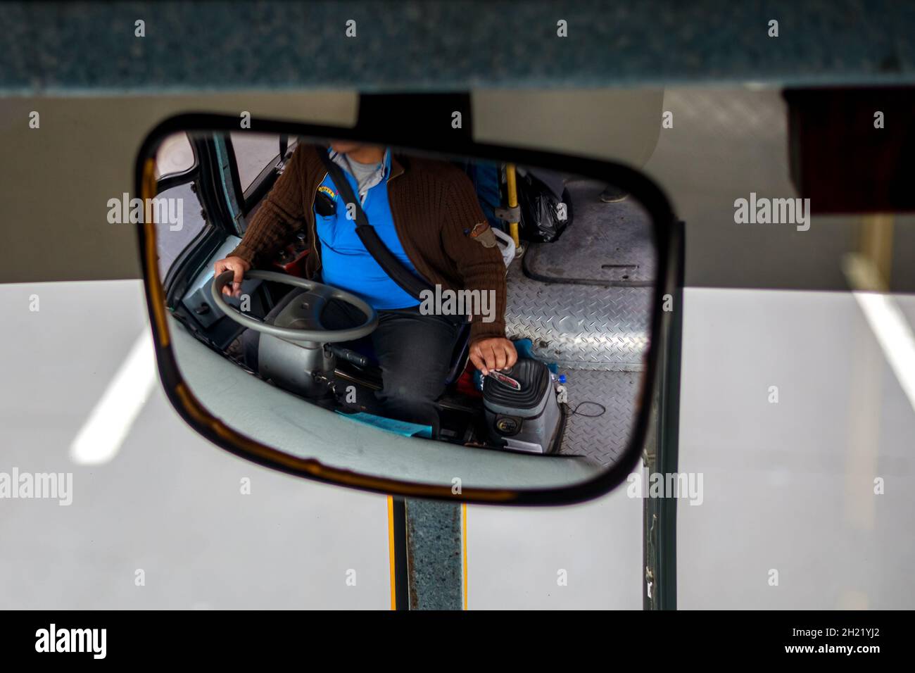 A reflection into a mirror of a bus driver in Lima, Peru during daytime. Stock Photo