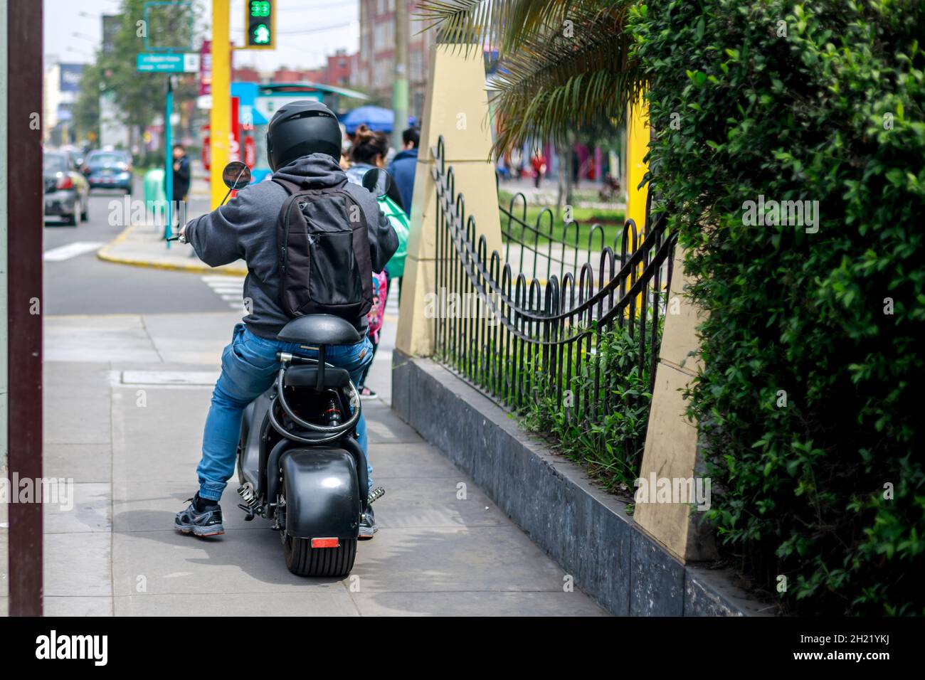 A person riding an electrical motorcycle on a city sidewalk during daytime. Stock Photo