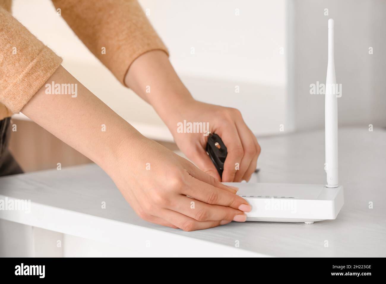 Woman inserting ethernet wire into wi-fi router on table in room Stock ...