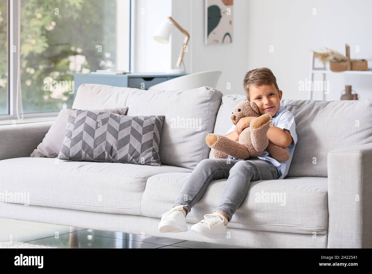 Cute little boy hugging teddy bear on sofa in living room Stock Photo ...