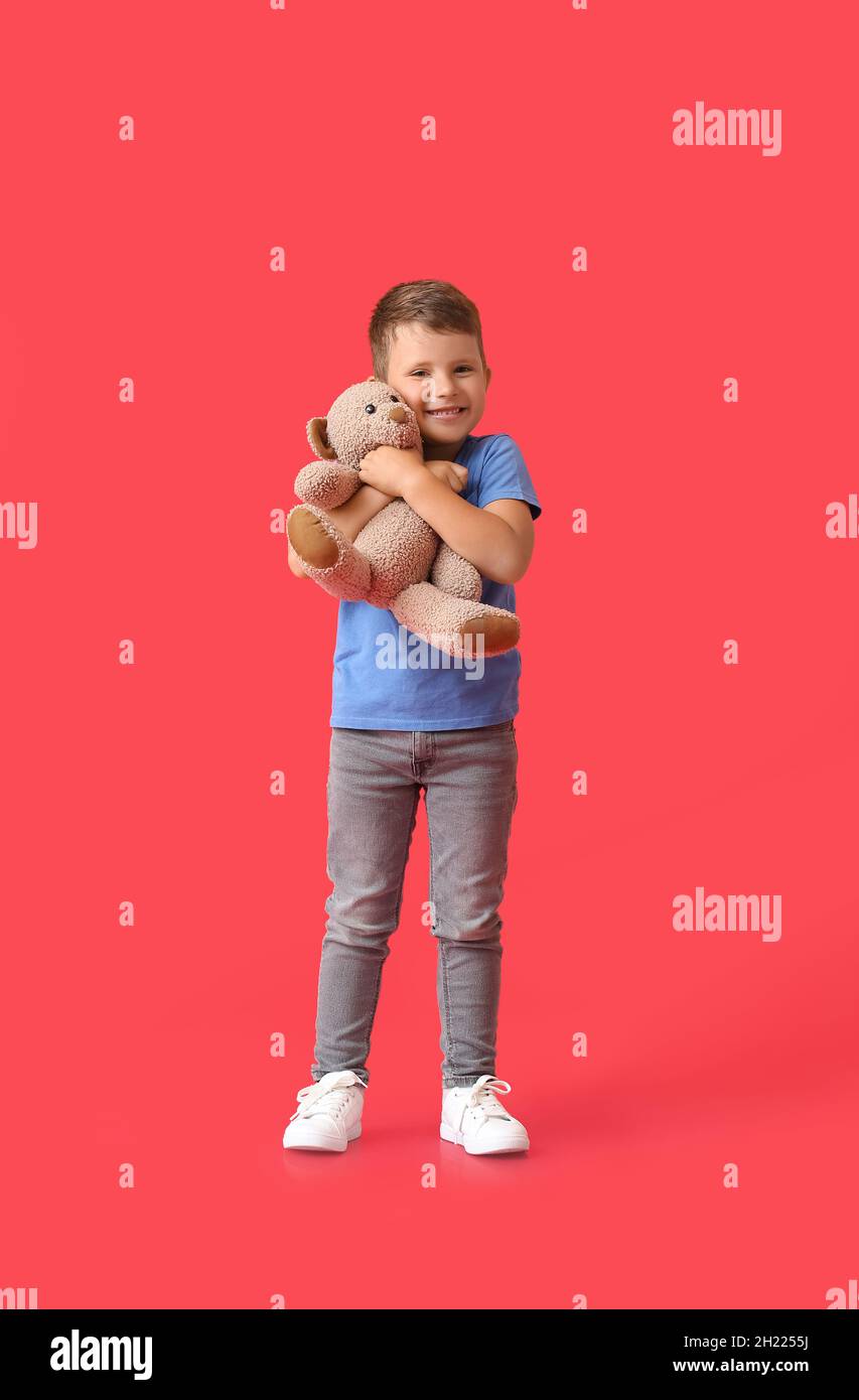 Cute little boy hugging teddy bear on red background Stock Photo - Alamy