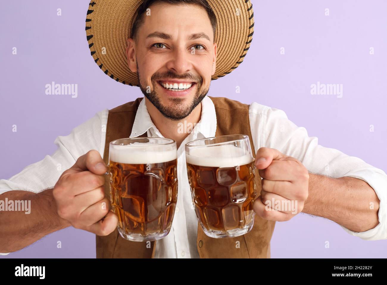 Young man in traditional German clothes with beer on lilac background