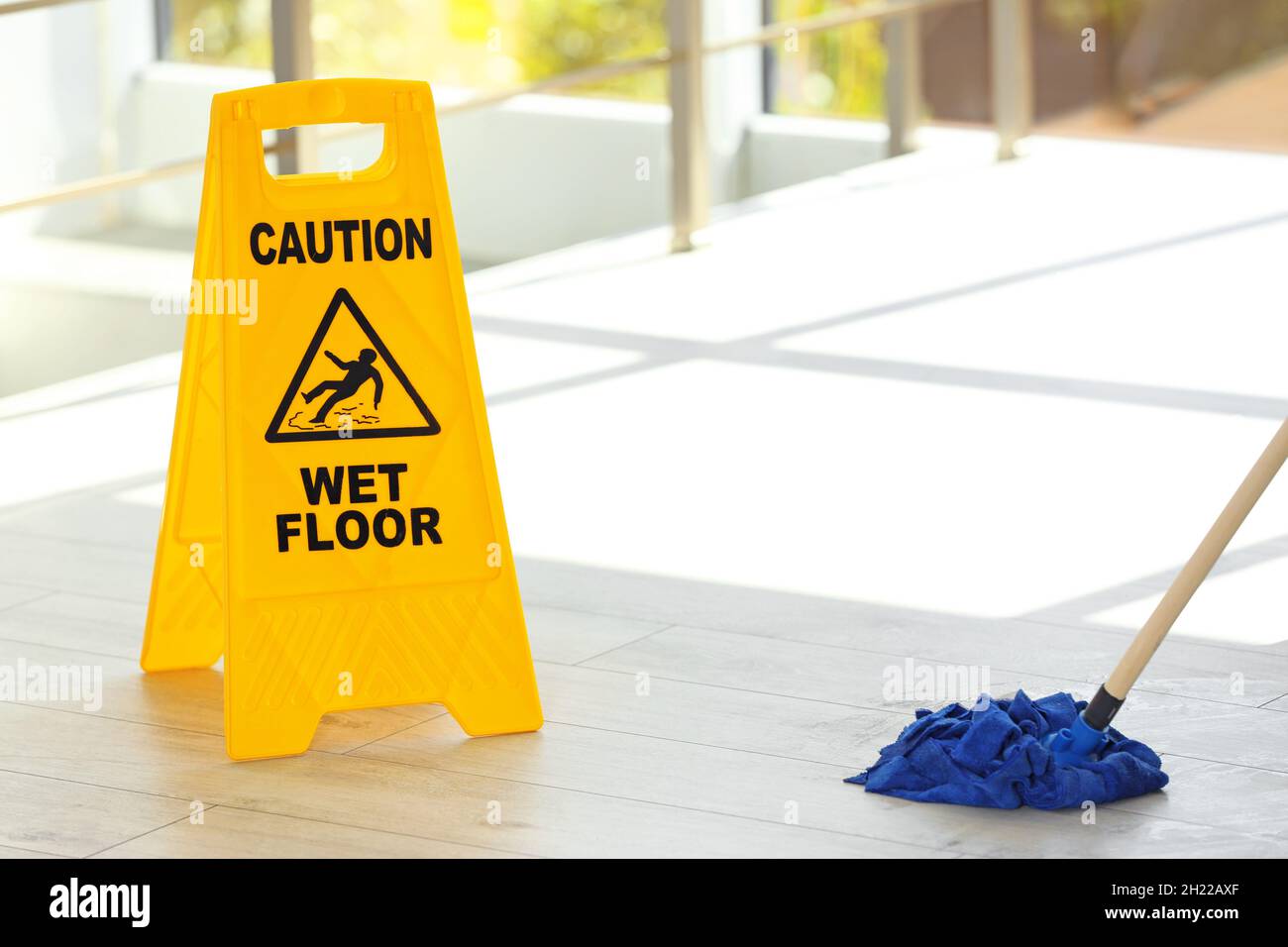 Safety sign with phrase Caution wet floor and mop, indoors. Cleaning