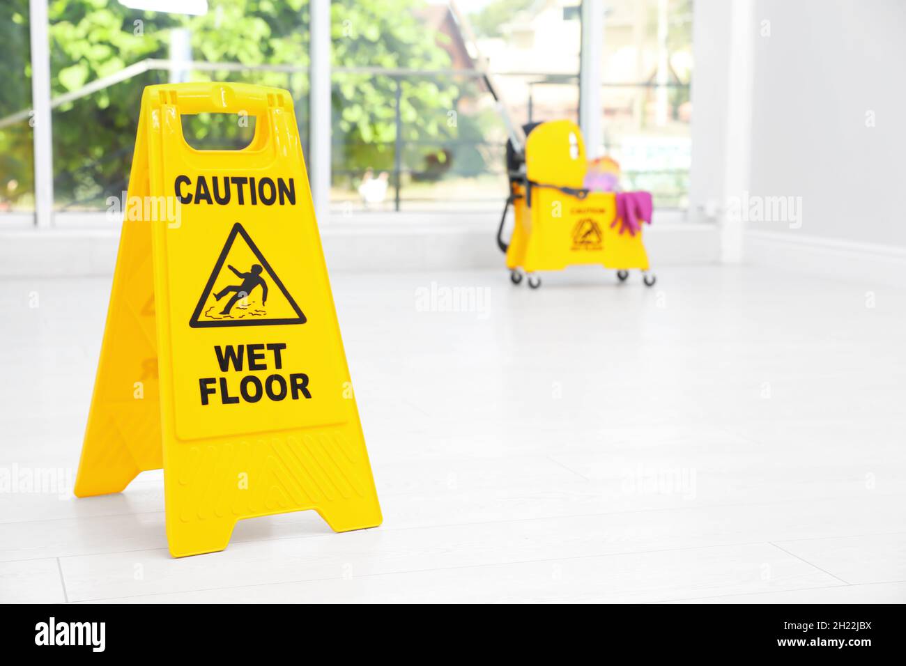 Safety sign with phrase "CAUTION WET FLOOR" and mop bucket on floor