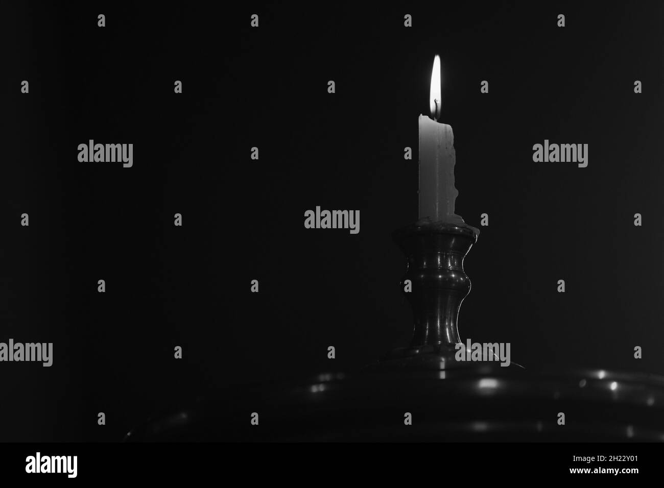 Closeup shot of a lit candle on a metal stand isolated on a dark background Stock Photo