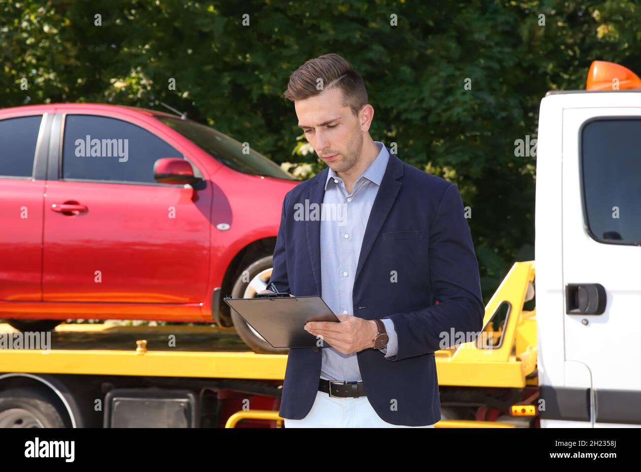 Man with clipboard near tow truck and broken car outdoors Stock Photo