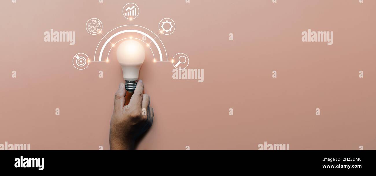 hand holding light bulb on pink background with icons brainstorming and business sources icon, innovation and creative concept Stock Photo