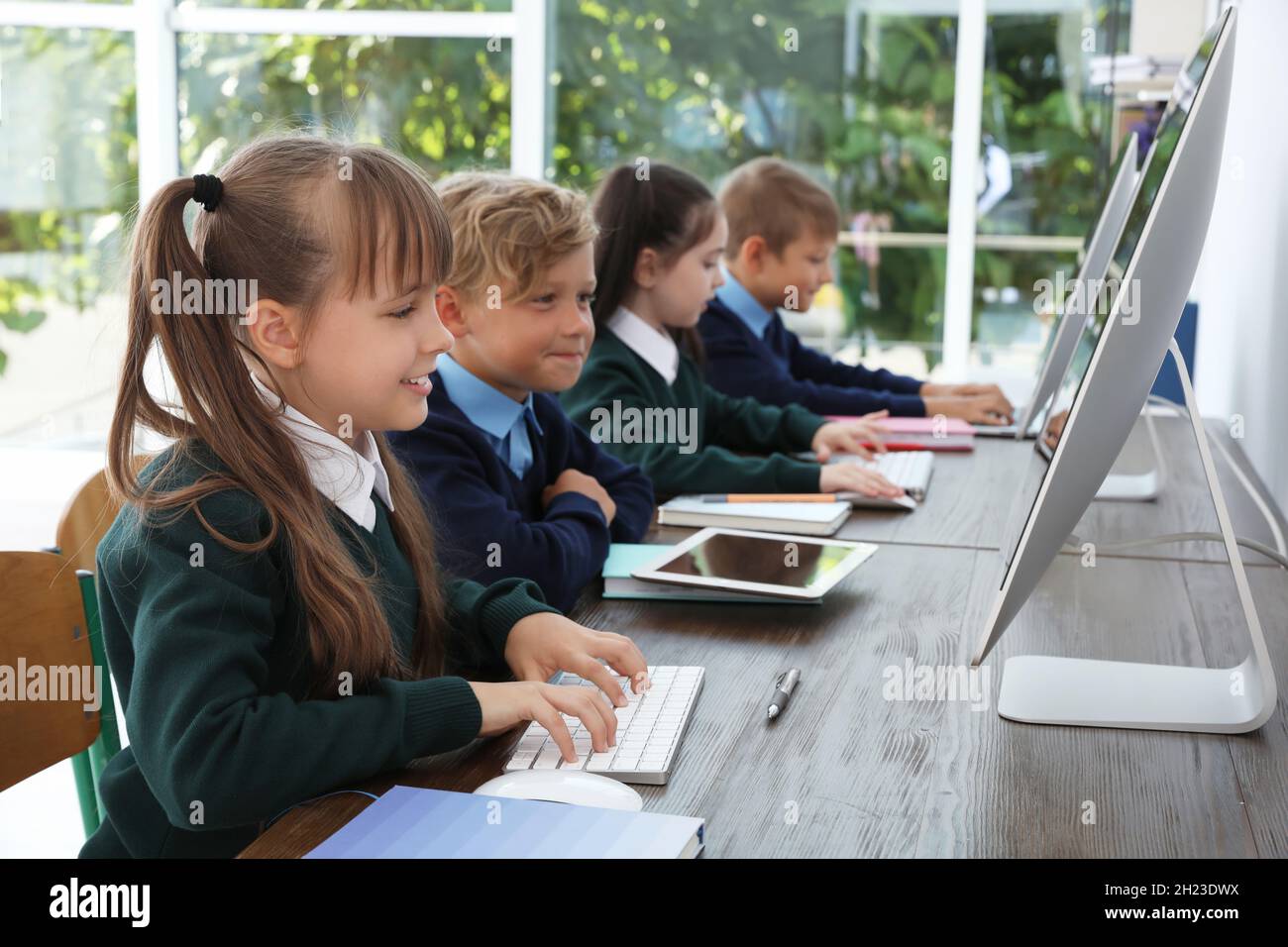 Little children in stylish school uniform at desks with computers Stock
