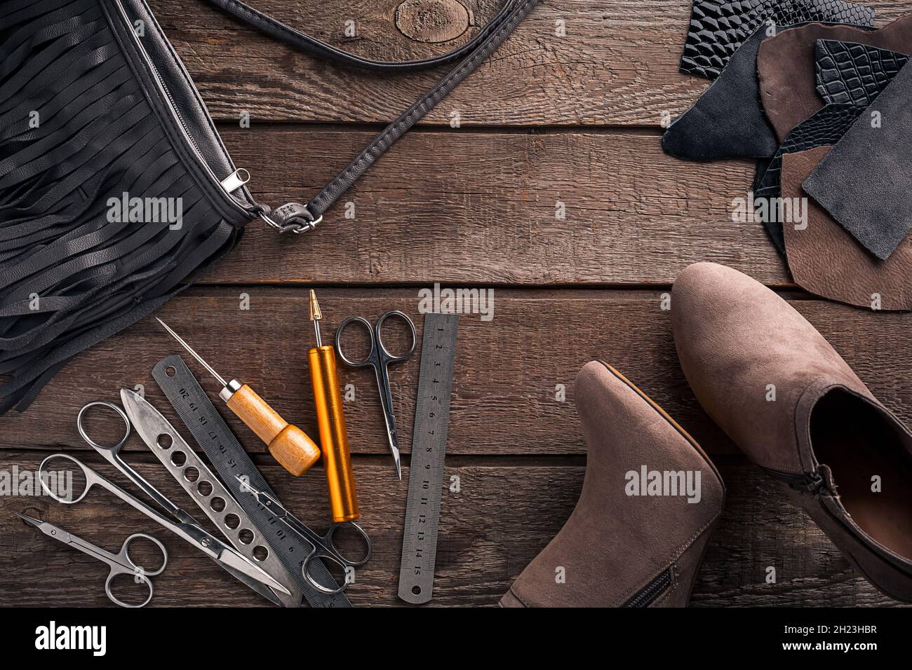 Leather craft or leather working. Selected pieces of beautifully colored or  tanned leather on leather craftman's work desk . Piece of hide and working  tools on a work table. Stock Photo