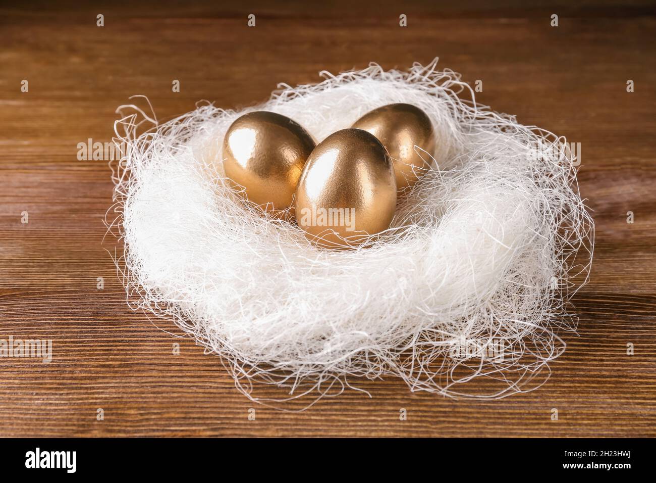Golden eggs in nest on wooden table. Pension planning Stock Photo - Alamy