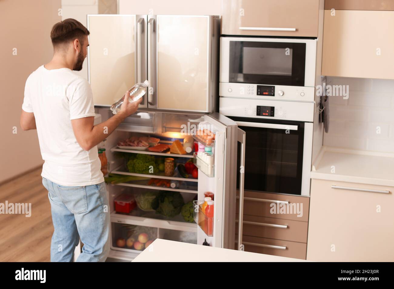 Young man taking bottle of water from refrigerator in kitchen Stock