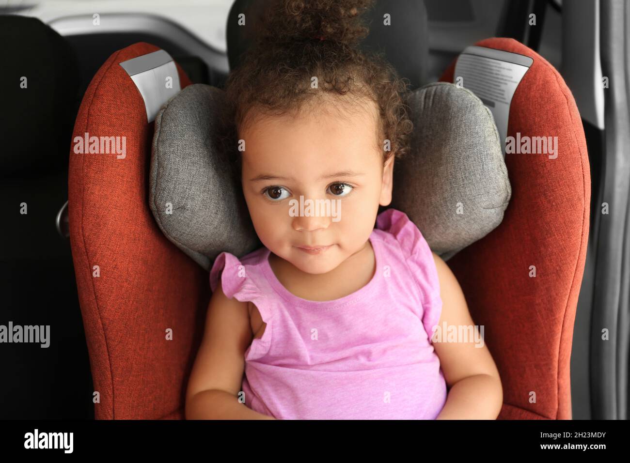 Little AfricanAmerican girl in child safety seat inside of car Stock