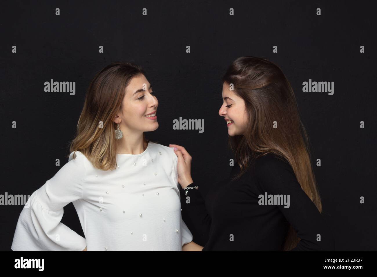 Portrait of two happy women friends with loving gestures laughing on a black background - Concept of friendship Stock Photo