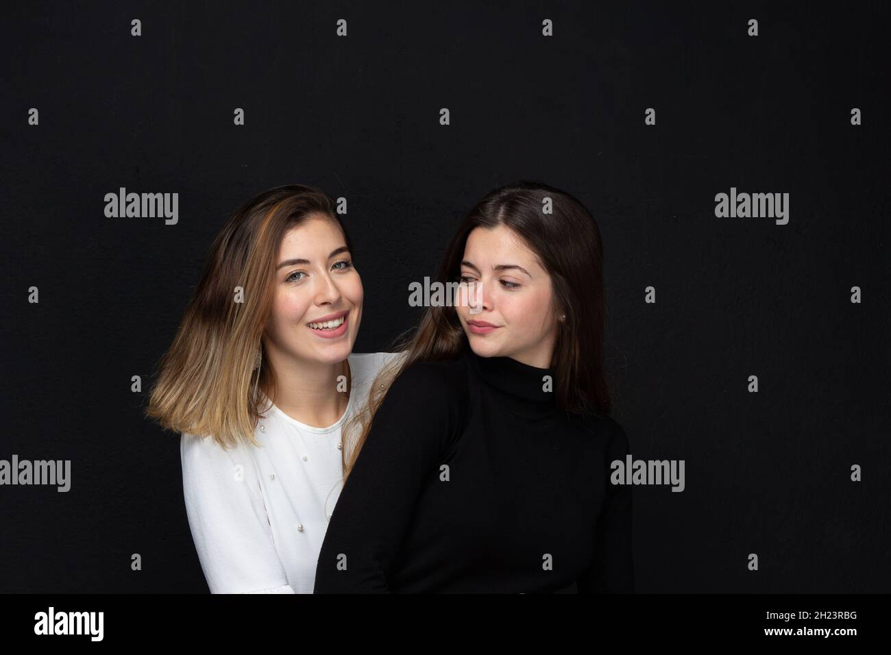 Portrait of two happy women friends with loving gestures laughing on a black background - Concept of friendship Stock Photo