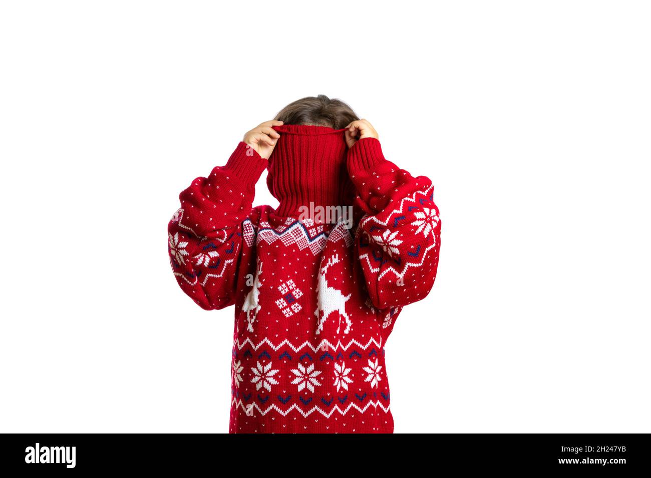 portrait of child in oversize red knitted Christmas sweater with reindeer hiding face in collar, isolated on white background Stock Photo