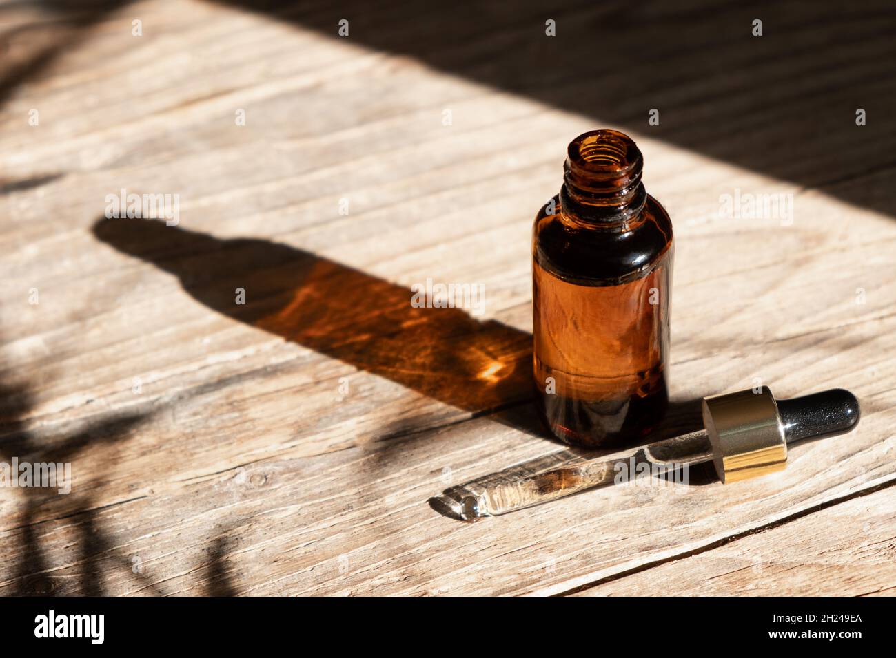 Open amber glass dropper bottle with metallic lid and a pipette on a wooden background. Natural cosmetics concept, natural essential oil. Stock Photo