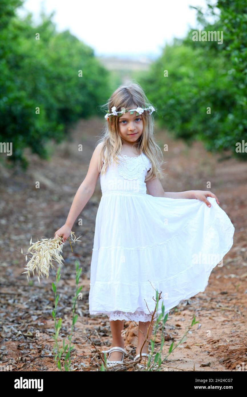 Young girl of six, in white dress and a wreath of flowers on her head ...