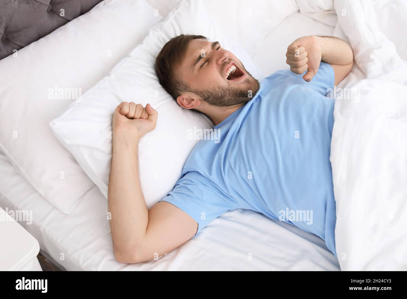 Young happy man waking up after sleeping in bed at home. Early ...