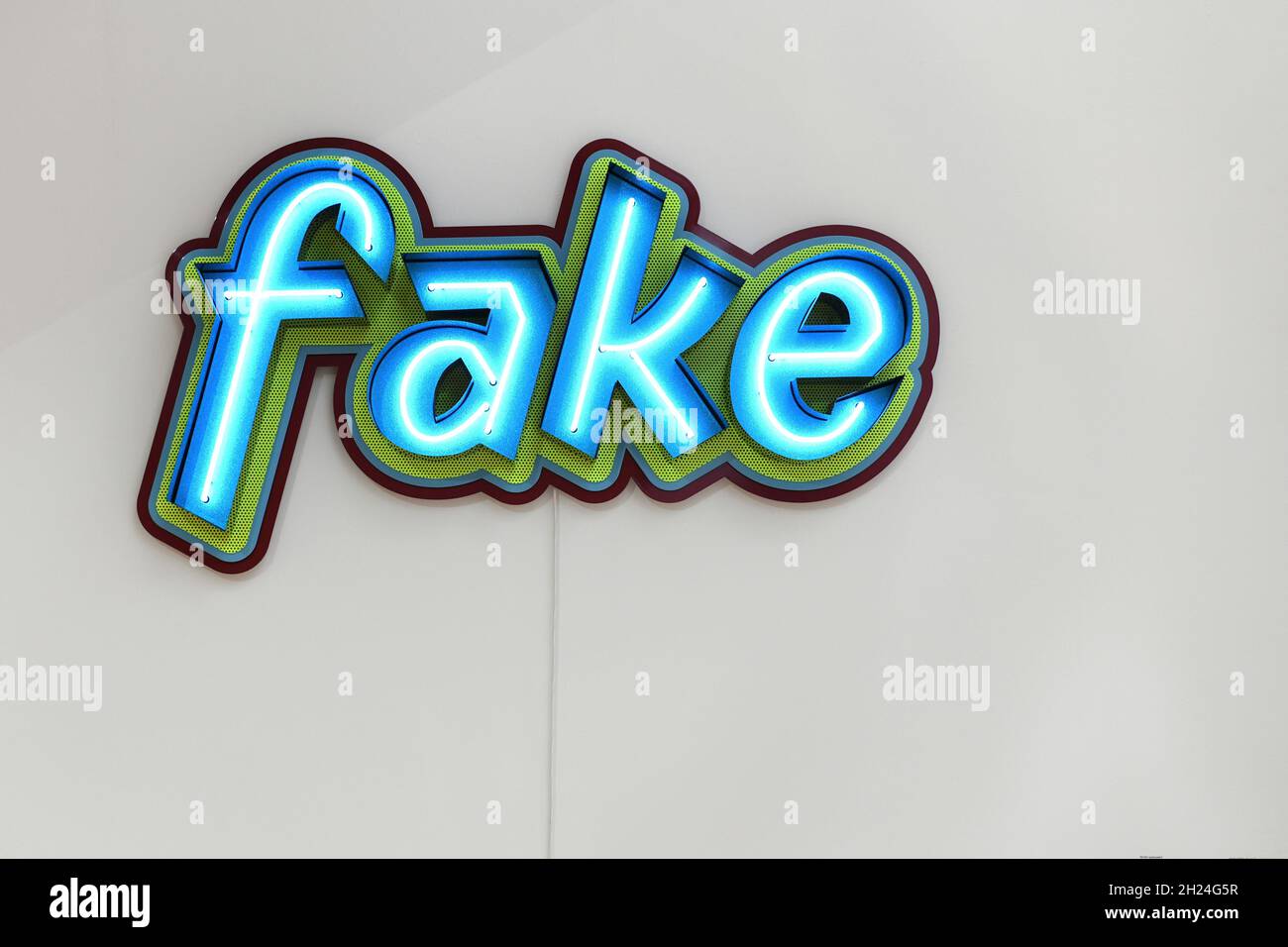 Neonleuchte an einer Wand mit der Aufschrift „Fake“ - Neon light on a wall that reads 'Fake' Stock Photo
