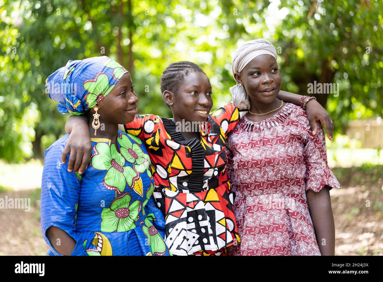 Three beautiful black African adolescent girls in colourful traditional outfit embracing each other; friendship concept Stock Photo