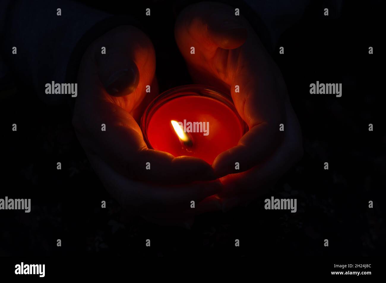 A red burning candle between a woman's palms. The woman shelters the
