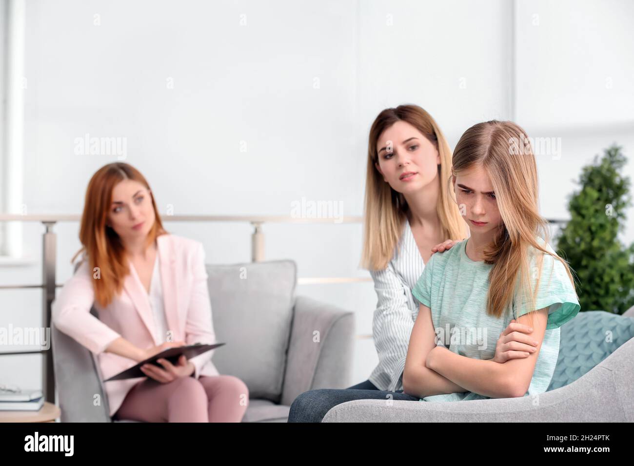 Young female psychologist working with teenage girl and her mother in