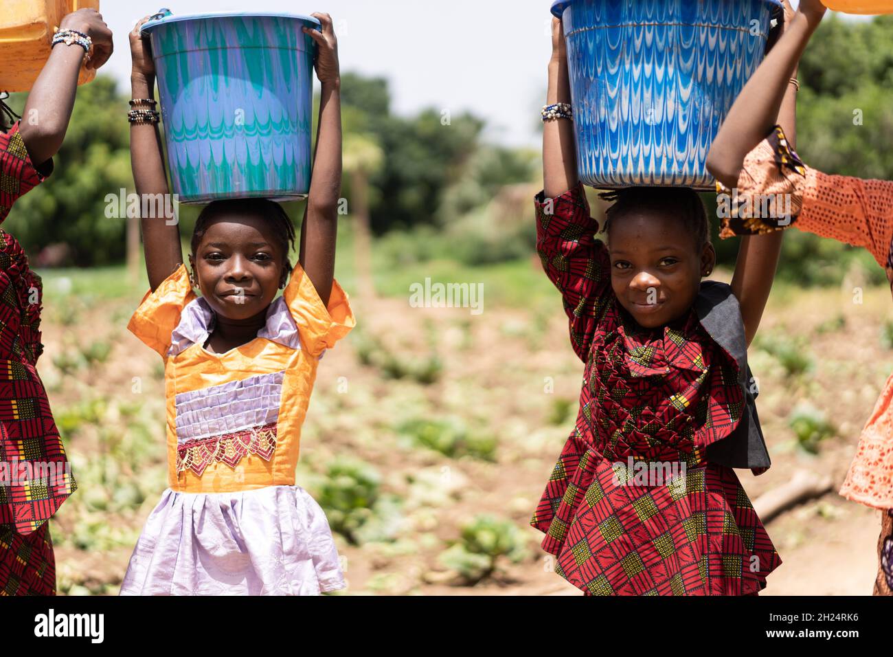 Closeup of two small black African girls carrying blue water buckets on their heads; child labour concept Stock Photo