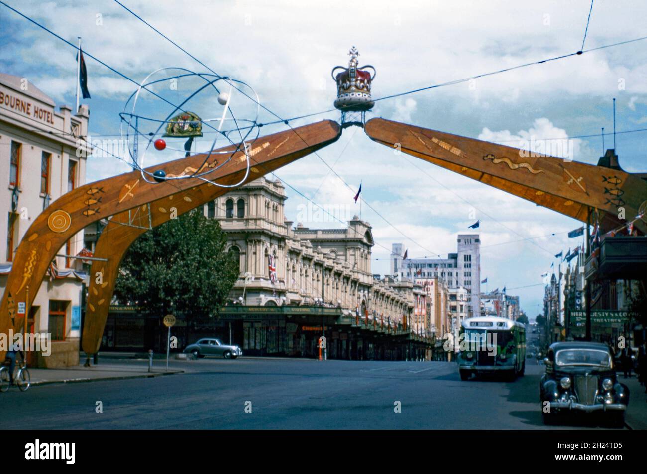 A commemorative arch in the shape of four boomerangs in Bourke Street, Melbourne, Victoria, Australia in 1954. It was erected to celebrate the Royal visit of Queen Elizabeth II on her Coronation Tour of the country. The imposing arch has an interesting design, with indigenous Aboriginal art topped with the royal crown (it would probably not be politically correct to mix the two in that way today). In front is an ‘atomic’ style hanging sculpture/mobile. The same arch was first used in Sydney for the Queen’s visit to that city. It was then swiftly moved to Melbourne – a vintage 1950s photograph. Stock Photo