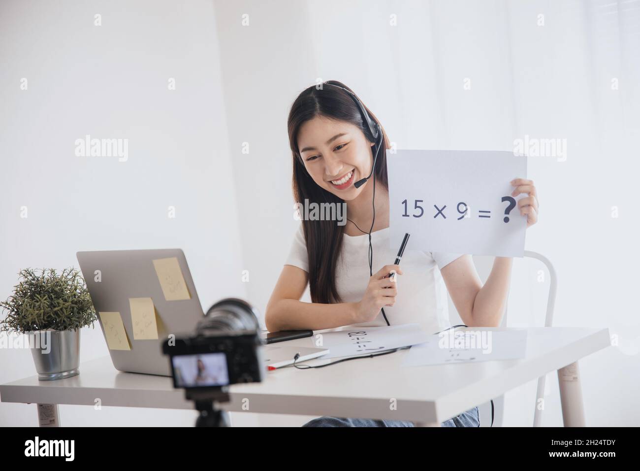 Young beautiful Asian teacher woman teach math online and look at laptop to chat with student in front of camera during quarantine and work from home. Stock Photo