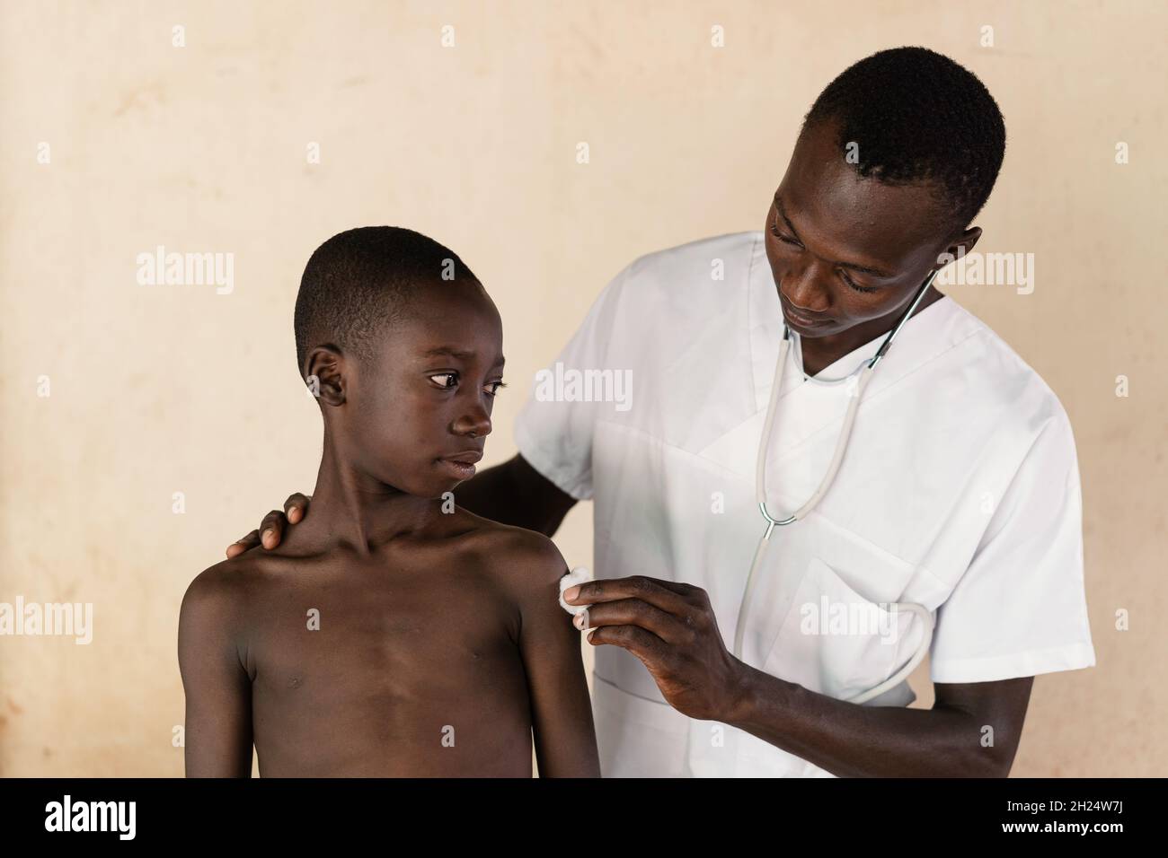 In this image, a doctor is disinfecting the injection site on a black boy's arm after malaria vaccination in West Africa Stock Photo