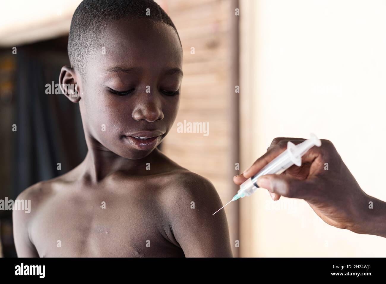 Black nurse explaining injection tool to a young attentive looking African schoolboy during antimalarial vaccination Stock Photo