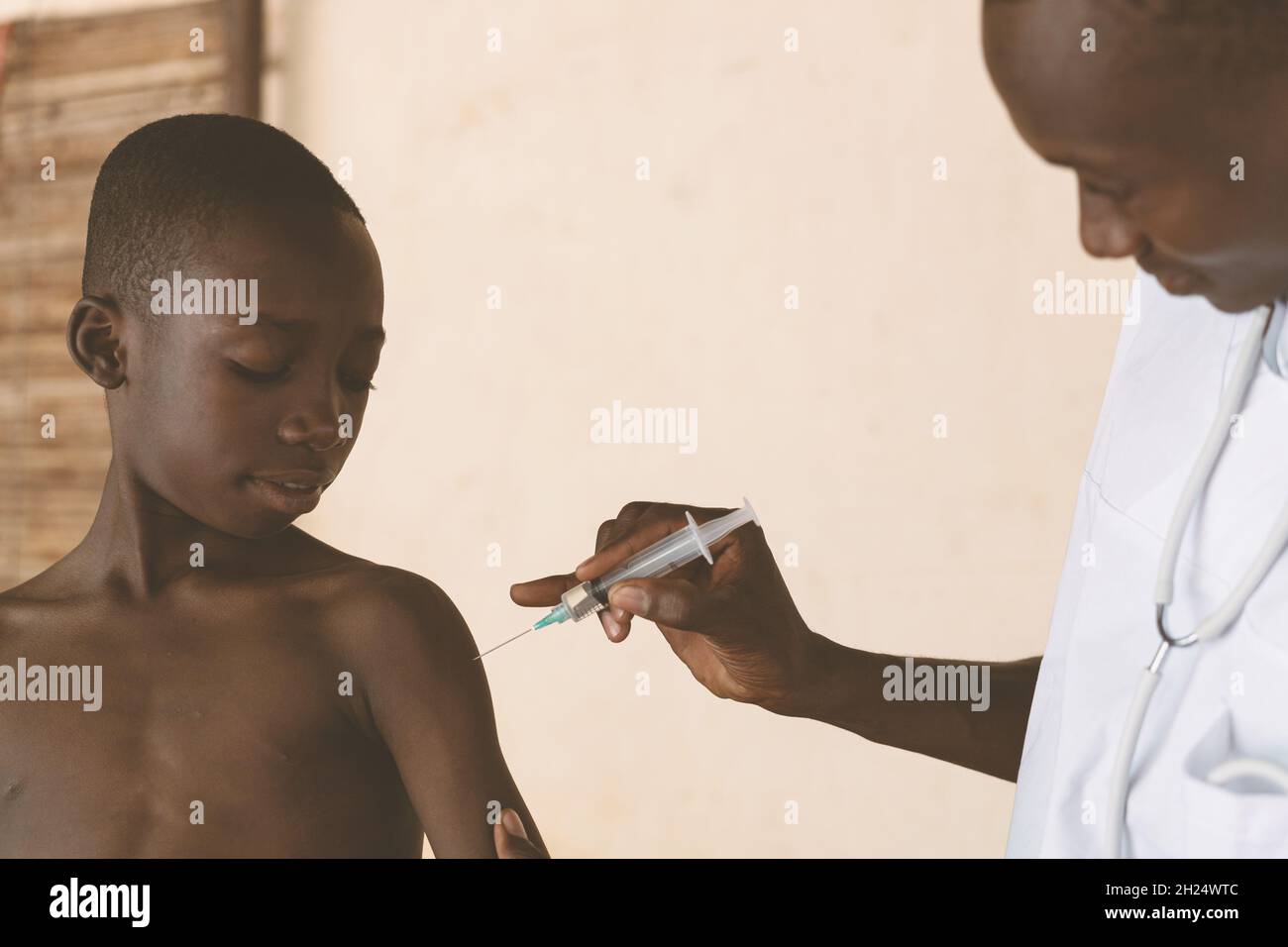 In this image, a doctor is explaing to a small confident looking black boy what happens during malaria vaccination Stock Photo