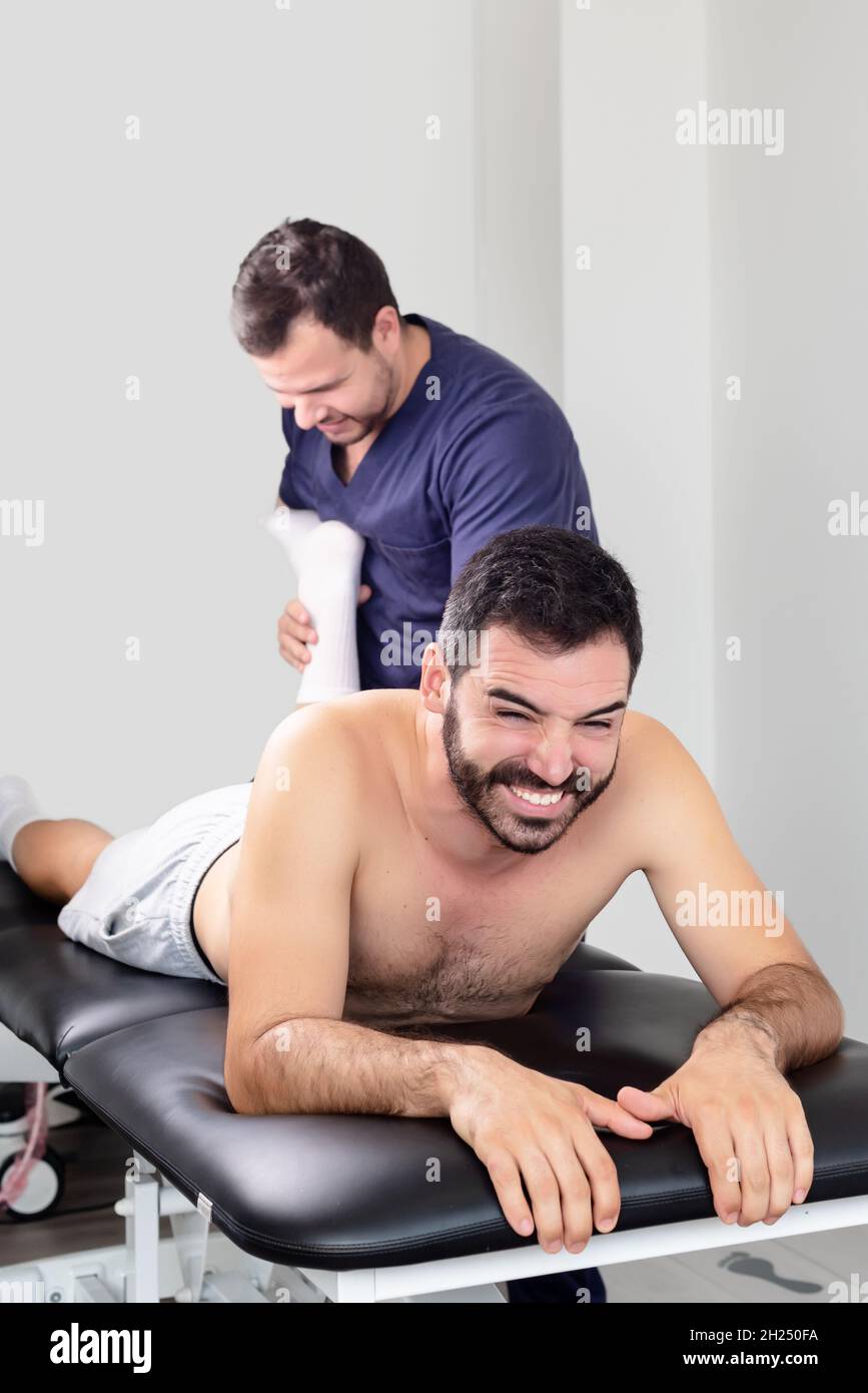 Patient lying on a stretcher feeling pain when physiotherapist flexes his leg Stock Photo