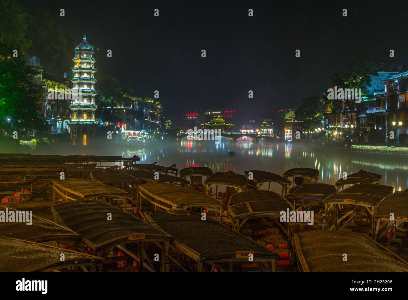 The Wanming Pagoda and covered boats on the Tuojiang River at night in Fenghuang, China. Stock Photo