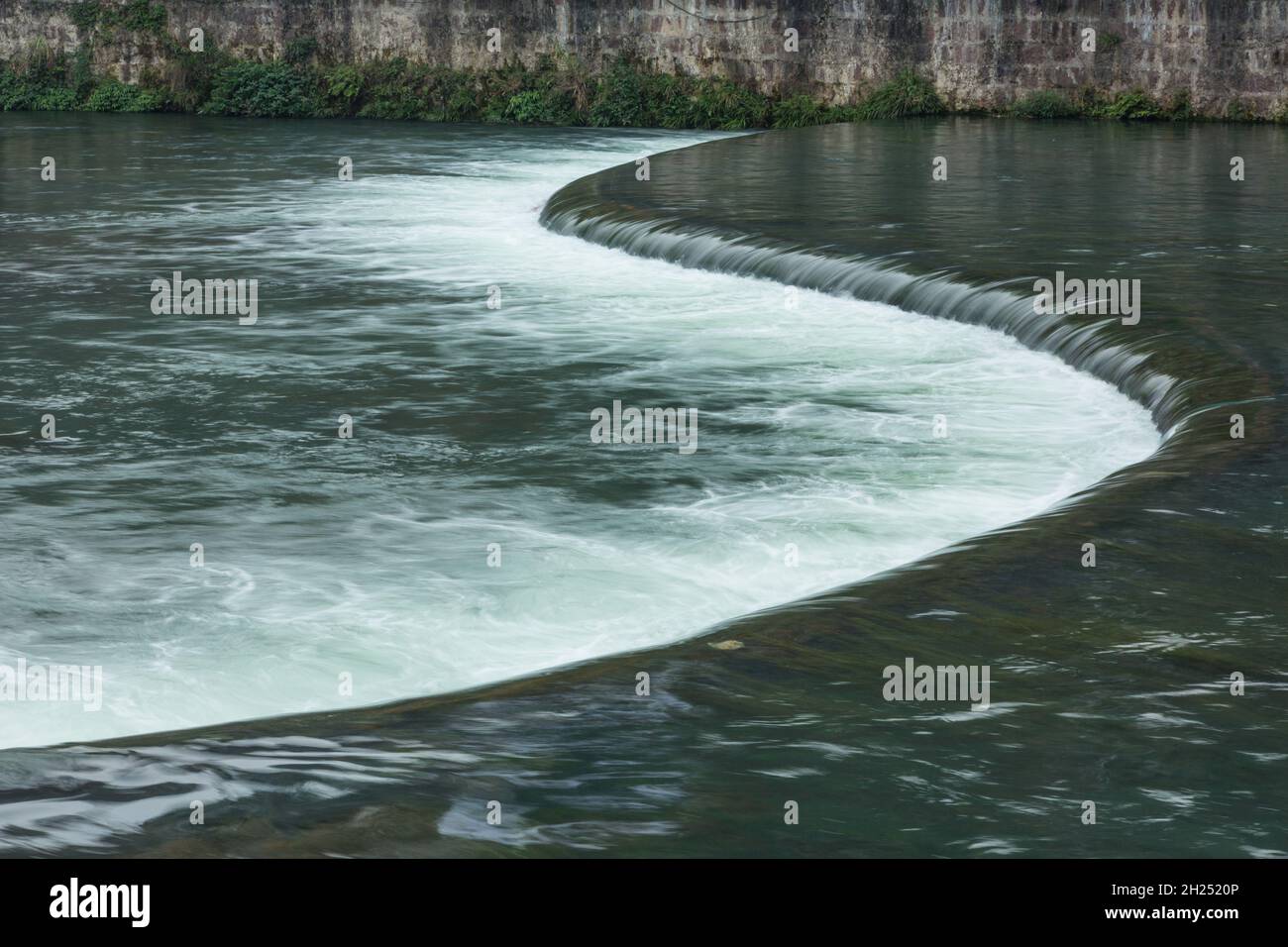 Water flows over an s-shaped weir across the Tuojiang River in Fenghuang, China. Stock Photo