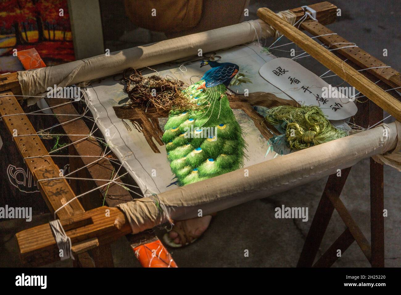 An elaborate needlework wallhanging of a peacock being hand-stitched in Guilin, China. Stock Photo