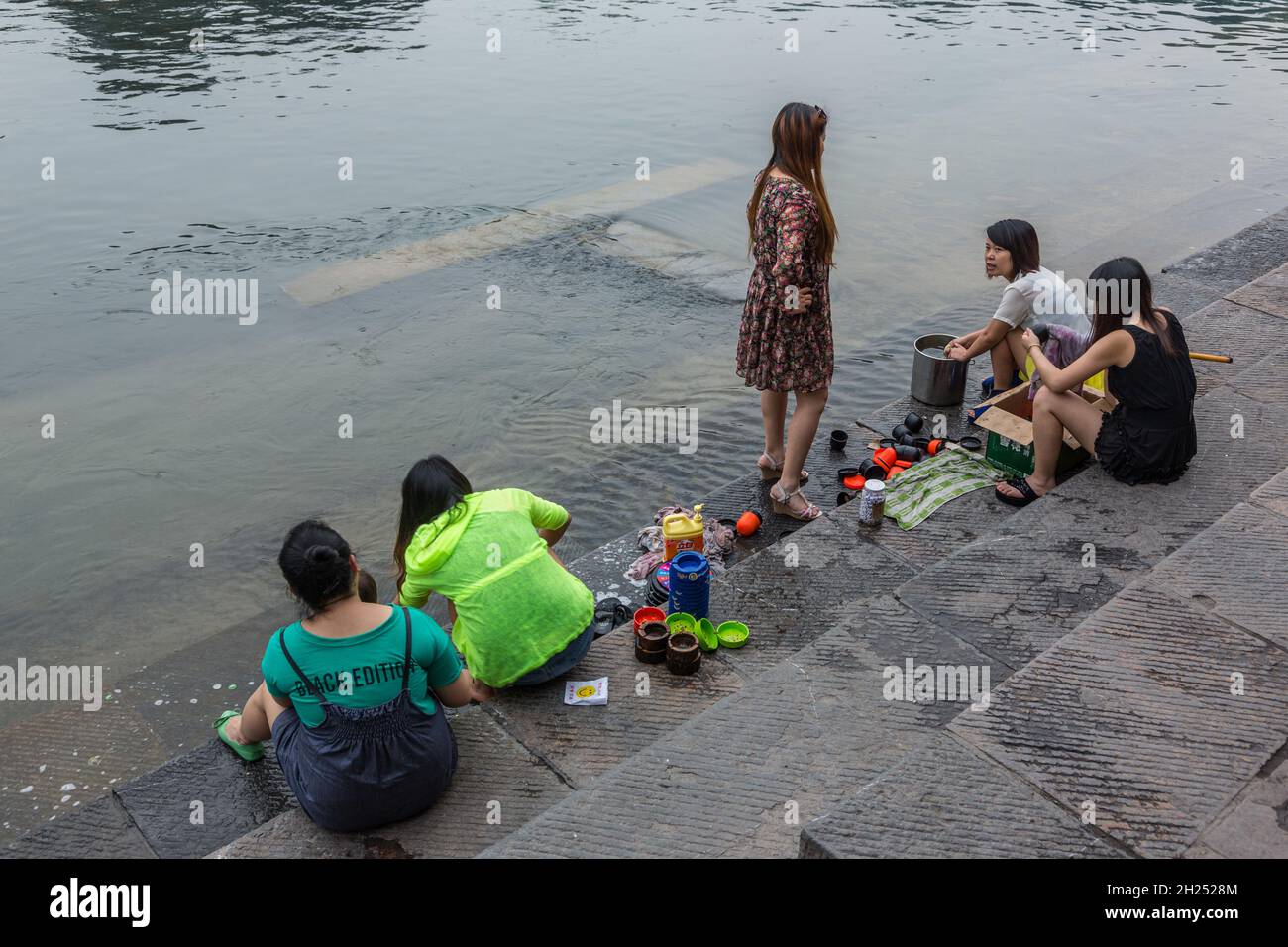 Women washing up dishes and ashtrays with river water on the bank of the Tuojiang River, Fenghuang, China. Stock Photo