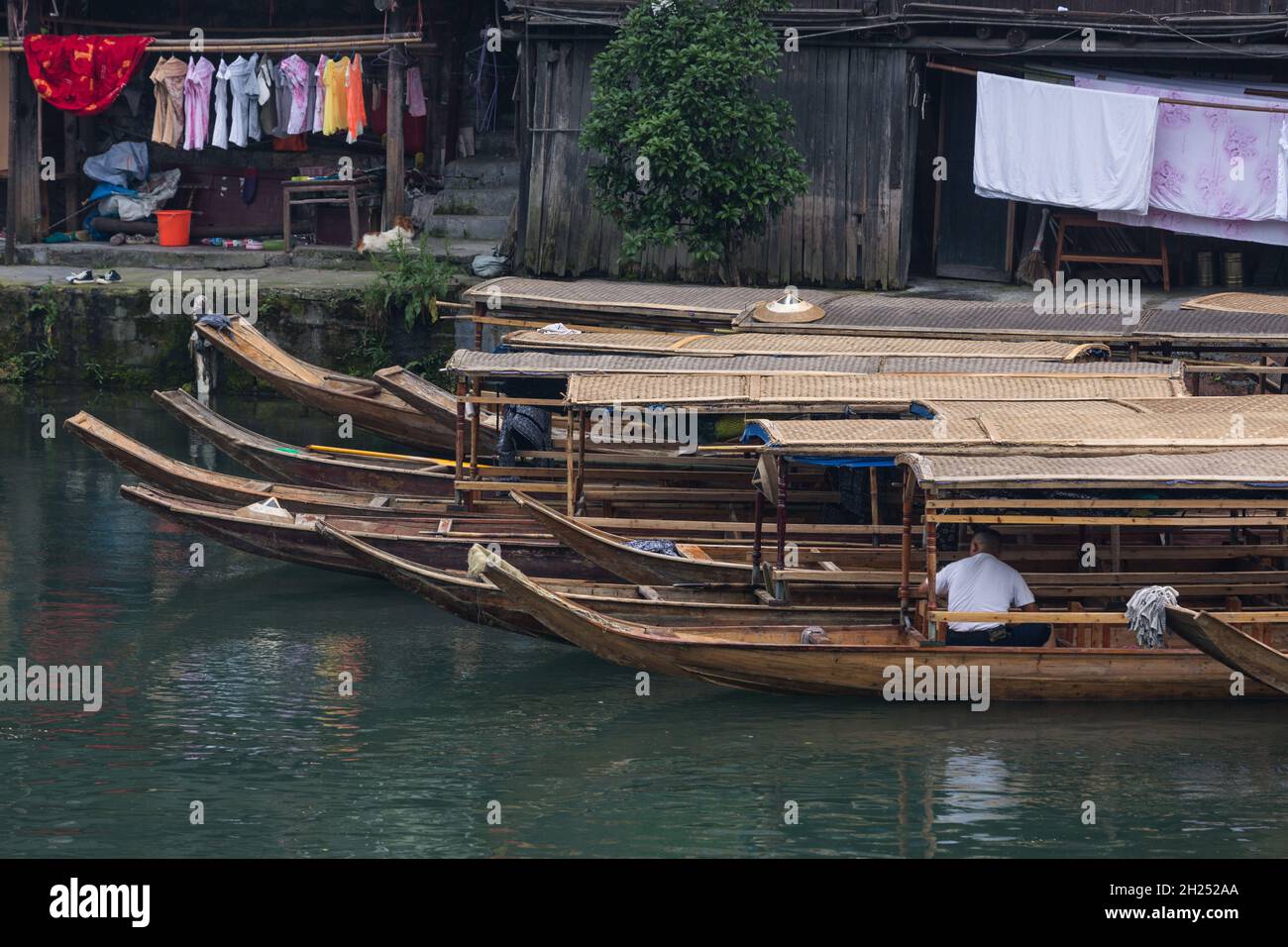 A boatman sits in his covered tour boat docked along the Tuojiang River in Fenghuang, China. Stock Photo