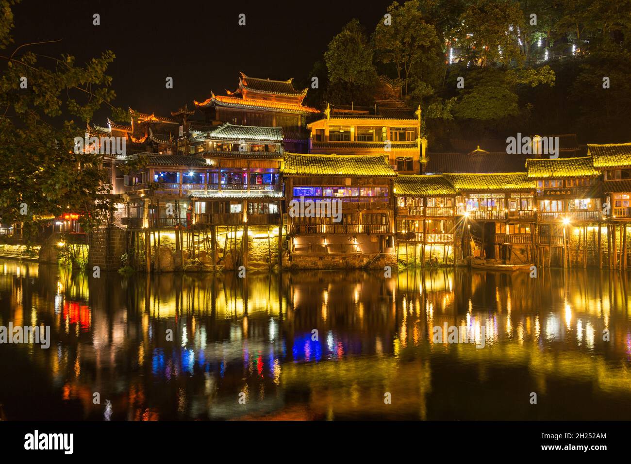 Traditional Diaojiao-style Chinese buildings lit up at night along the Tuojiang River in Fenghuang, China. Stock Photo