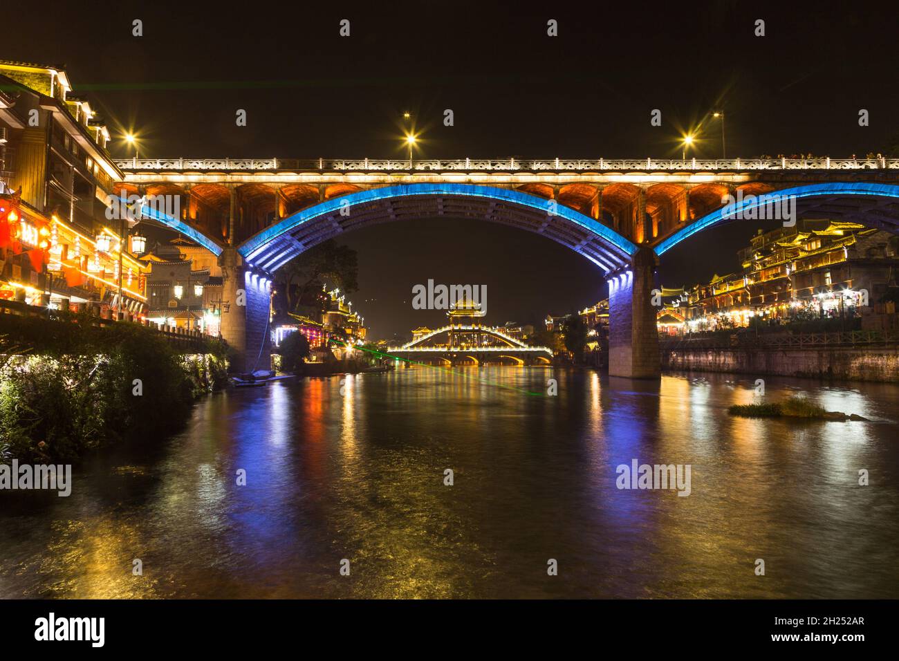 The hIghway bridge frames the Fenghuang Bridge lit up at night in Fenghuang, China. Stock Photo