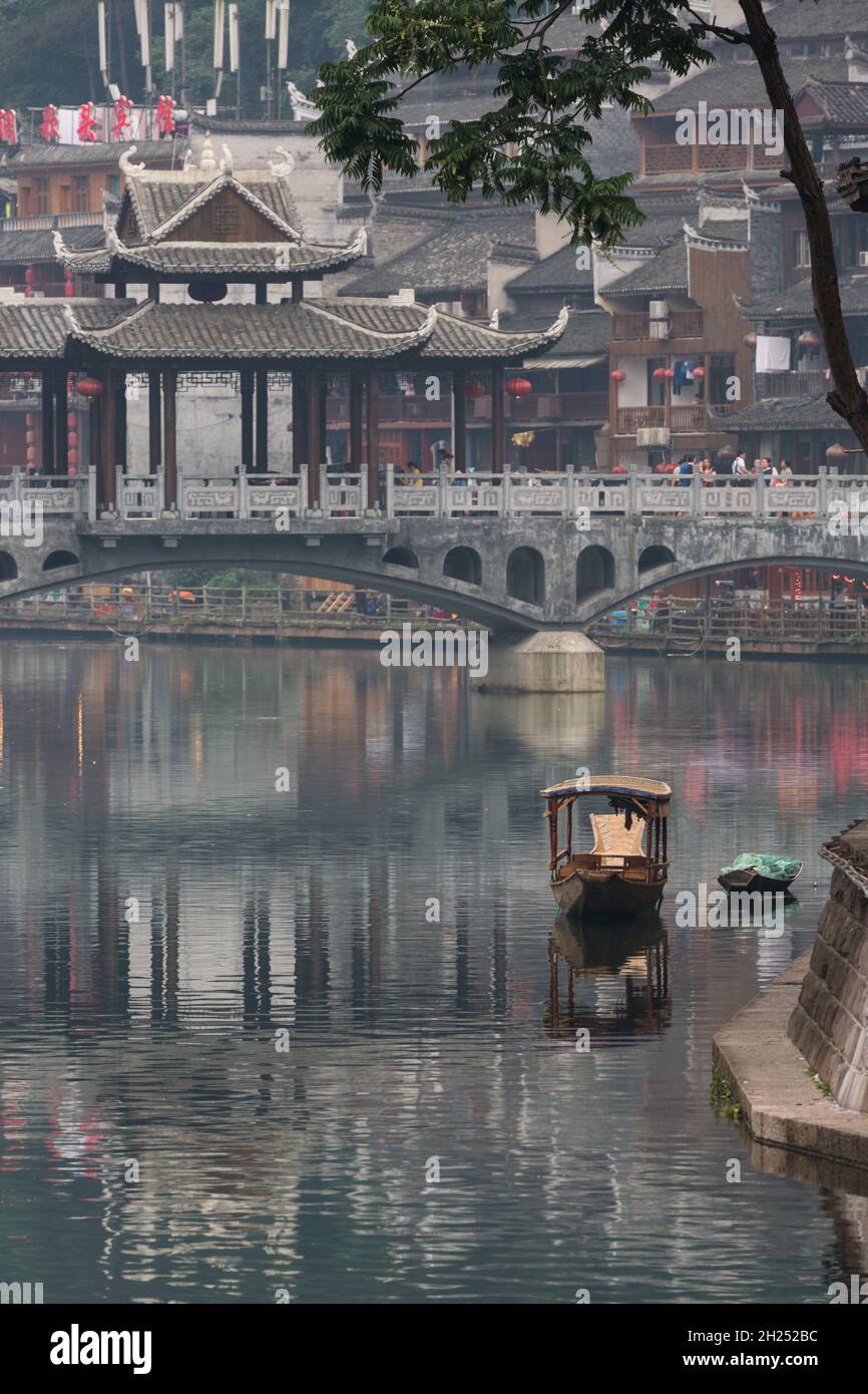 A boat on the Tuojiang River with a stone bridge behind in Fenghuang, China. Stock Photo