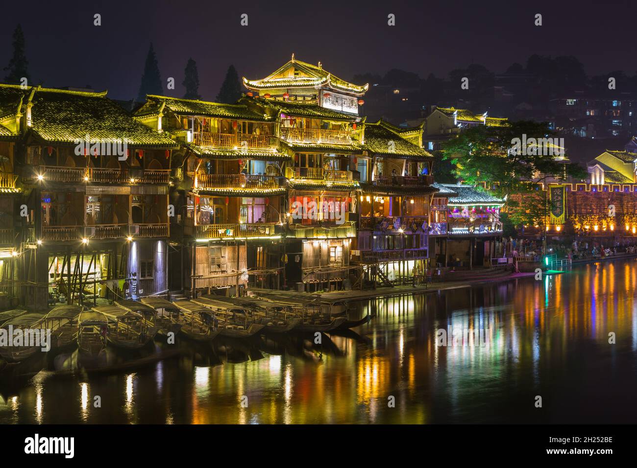 Traditional Diaojiao-style buildings on stilts lit up at night on the Tuojiang River in Fenghuang, China. Stock Photo